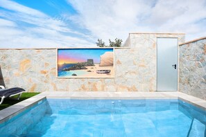 Une piscine avec un mur en pierre et une porte, ainsi qu’une fresque représentant une scène de plage.