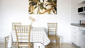 A dining area with a table set for two, a wall-mounted artwork, and a kitchen area with cabinets.