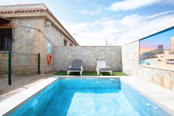 Une piscine avec deux chaises longues, un mur en pierre et une fresque murale.