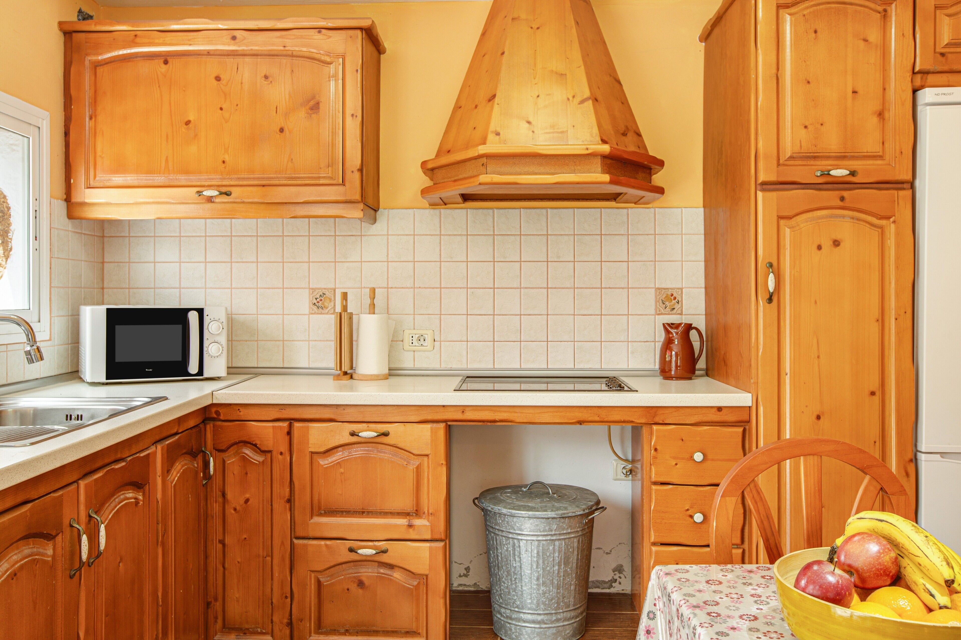 Una cucina con mobili in legno, un forno a microonde, un lavandino e un cestino.