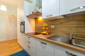 Une cuisine moderne dotée d’un évier en acier inoxydable, d’un plan de travail en bois et d’un présentoir à fruits.