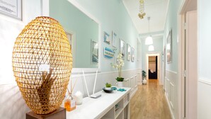 A hallway with a white reception desk, a large decorative lamp, framed artwork on the walls, and a wooden floor. - Vacation Apartment "Appartamento degiorgio8" with Terrace & Wi-Fi (ALGHERO)