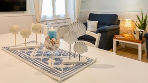A living room with a white table, decorative shells, a candle, and a blue and white rug. - Vacation Apartment "Appartamento degiorgio8" with Terrace & Wi-Fi (ALGHERO)