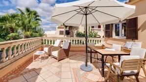 Une terrasse extérieure aménagée avec des meubles en osier, une table et un grand parasol.