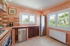 A compact kitchen with a dishwasher, refrigerator, and a window overlooking greenery.