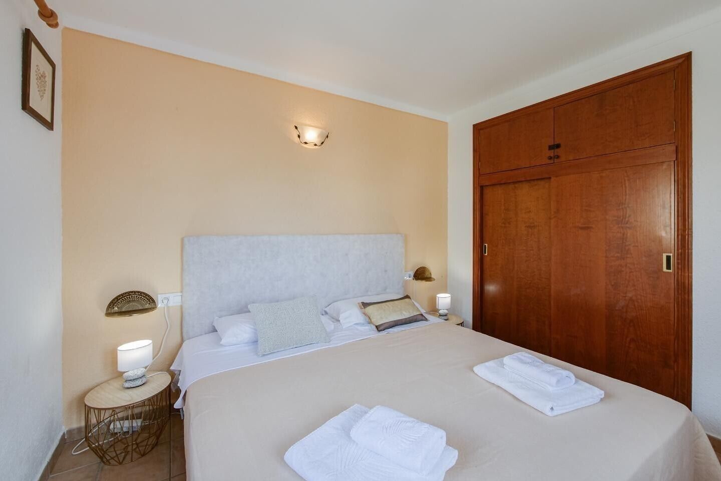 Une chambre à coucher avec un lit, des lampes de chevet, une armoire en bois et une petite table ronde avec une lampe.