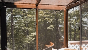 Une pièce chaleureuse avec une grande fenêtre, des meubles en osier et une vue sur les arbres.