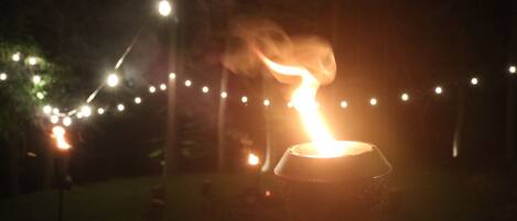 A candle in a glass holder outdoors at night with string lights in the background.