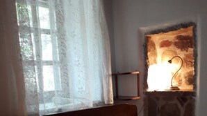 En säng med vita sängkläder, ett fönster med tunna gardiner och en vägglampa.
