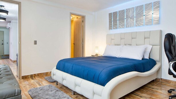 A modern bedroom with a white bed, blue bedding, and a grey rug. - 3 Bedroom PH Hot Tub Sliding Roof AC (Medellin)