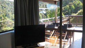 A balcony with a TV, wooden chairs, and a view of a forested area. - One week (7 to 14 Jan. 2023) in Club Paihia award winning resort  (Paihia)