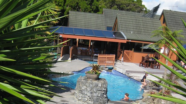 A swimming pool with a waterfall feature, surrounded by palm trees and a building with a sloped roof. - One week (7 to 14 Jan. 2023) in Club Paihia award winning resort  (Paihia)