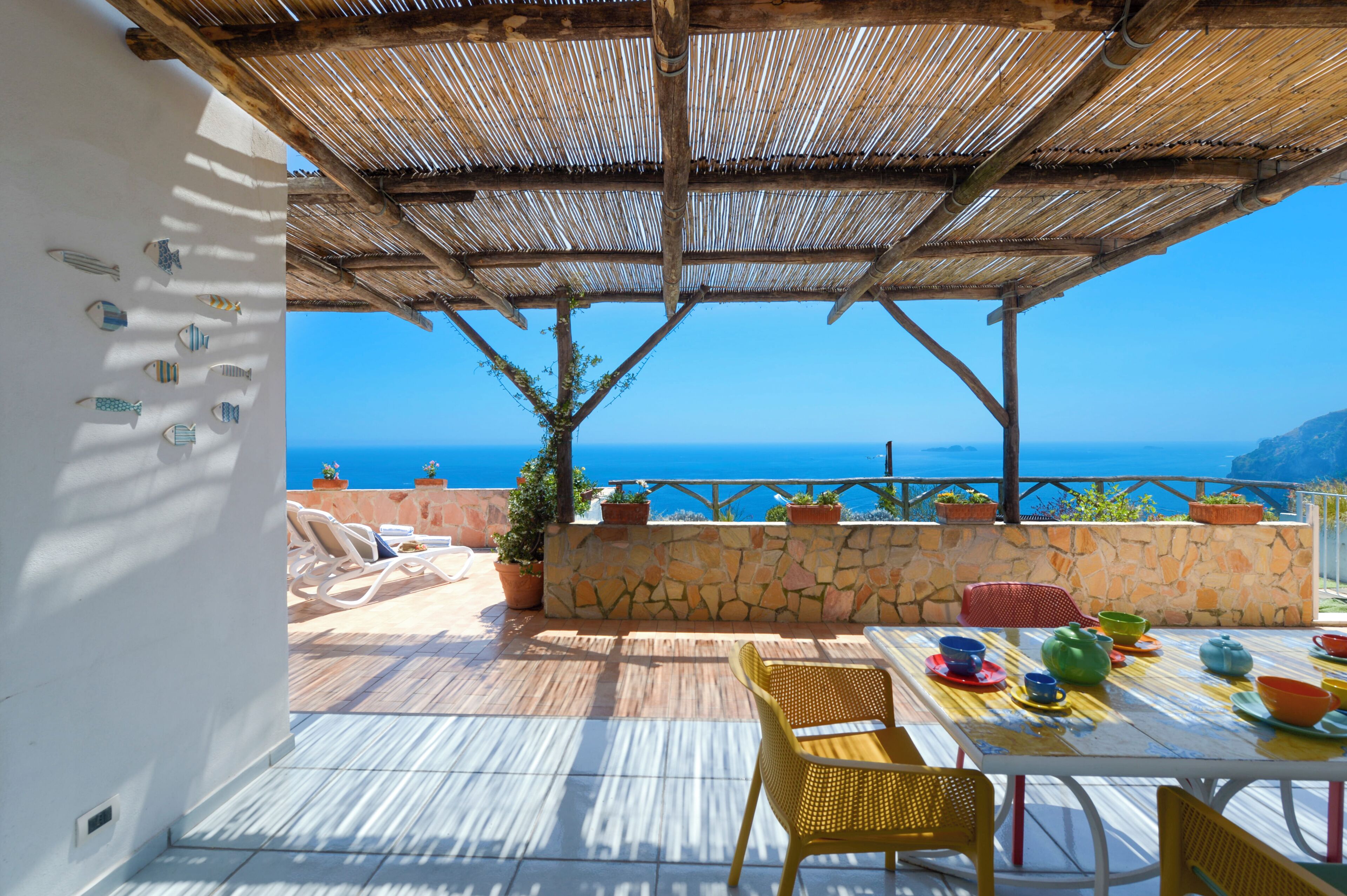 A terrace with a stone wall, a table with colorful plates, and a view of the sea.