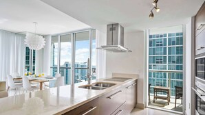 A modern kitchen with a large island, stainless steel appliances, and a view of the city through large windows. - Open Plan Brickell Suite with Workspace (Miami)