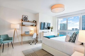 A modern bedroom with a bed, desk, chair, and a large window with a city view.