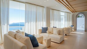 A spacious living area with a large window offering a view of the sea and mountains. - Apeiron Blue by Apeiron Hotels (Santorini)