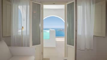 An open room with a view of the sea through a glass door, a white sofa, and a table with a vase.