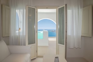 Habitación amplia con vistas al mar a través de un ventanal, un sofá blanco y una mesa con un florero.