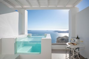 Un balcón con vista despejada al mar, una bañera de hidromasaje y una mesa con una botella y vasos.