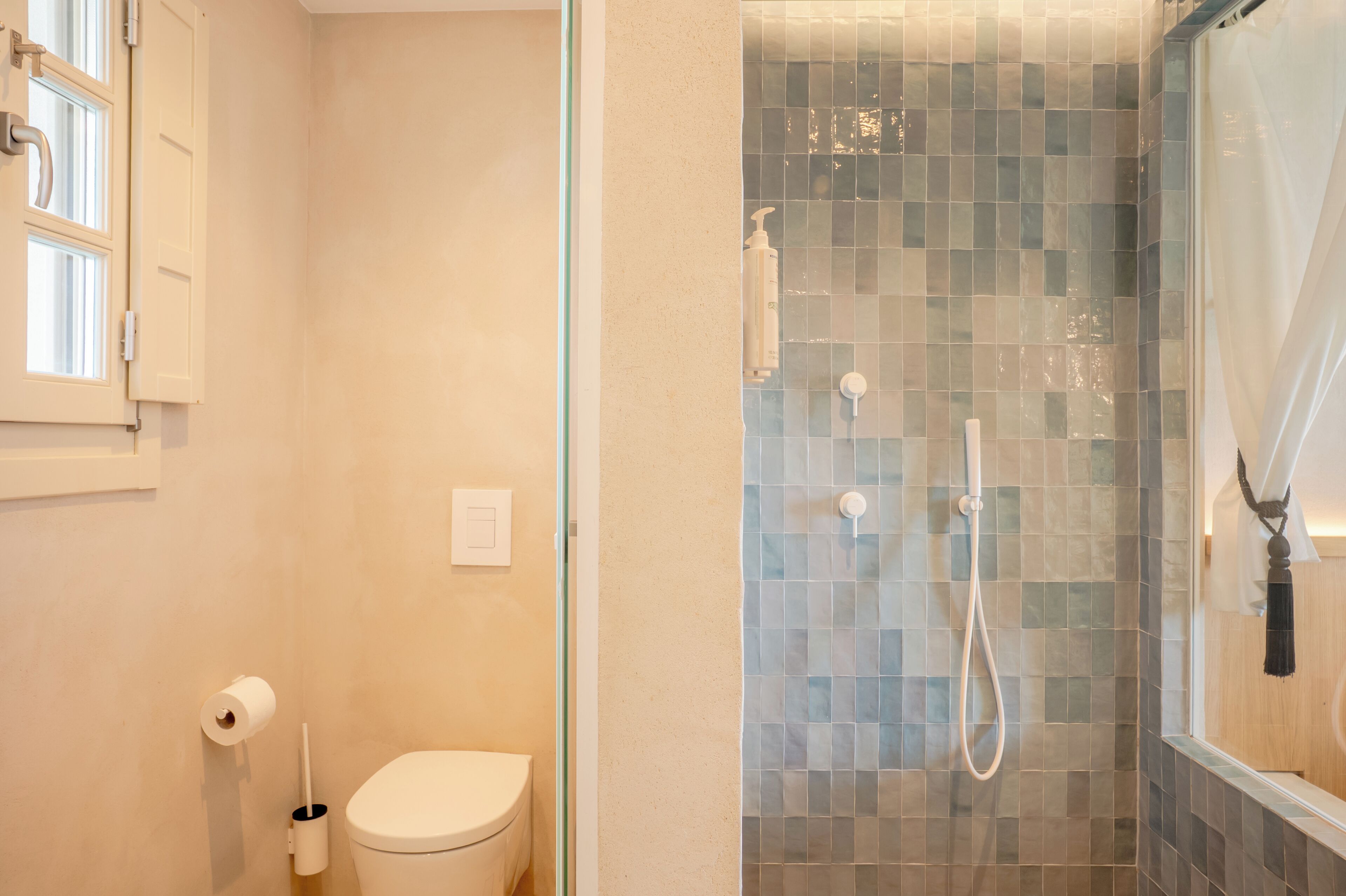 Un baño con inodoro, ducha con puerta de cristal y ventana con persianas.