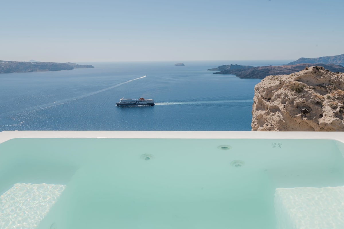 Vista de una extensa masa de agua con un crucero a lo lejos, un acantilado rocoso a la derecha y un cielo despejado.