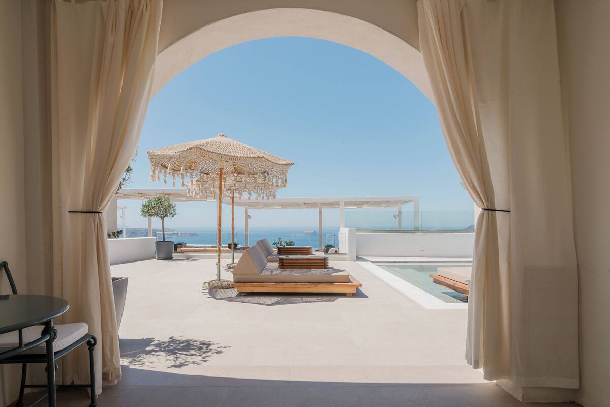 Una terraza con vista al mar, que cuenta con una zona de estar con toldo, una mesa y una planta en maceta.
