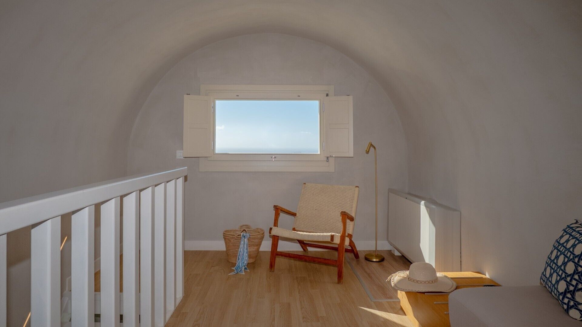 Una habitación pequeña en ático con techo inclinado, una ventana, una silla de madera, una lámpara de pie y un radiador.