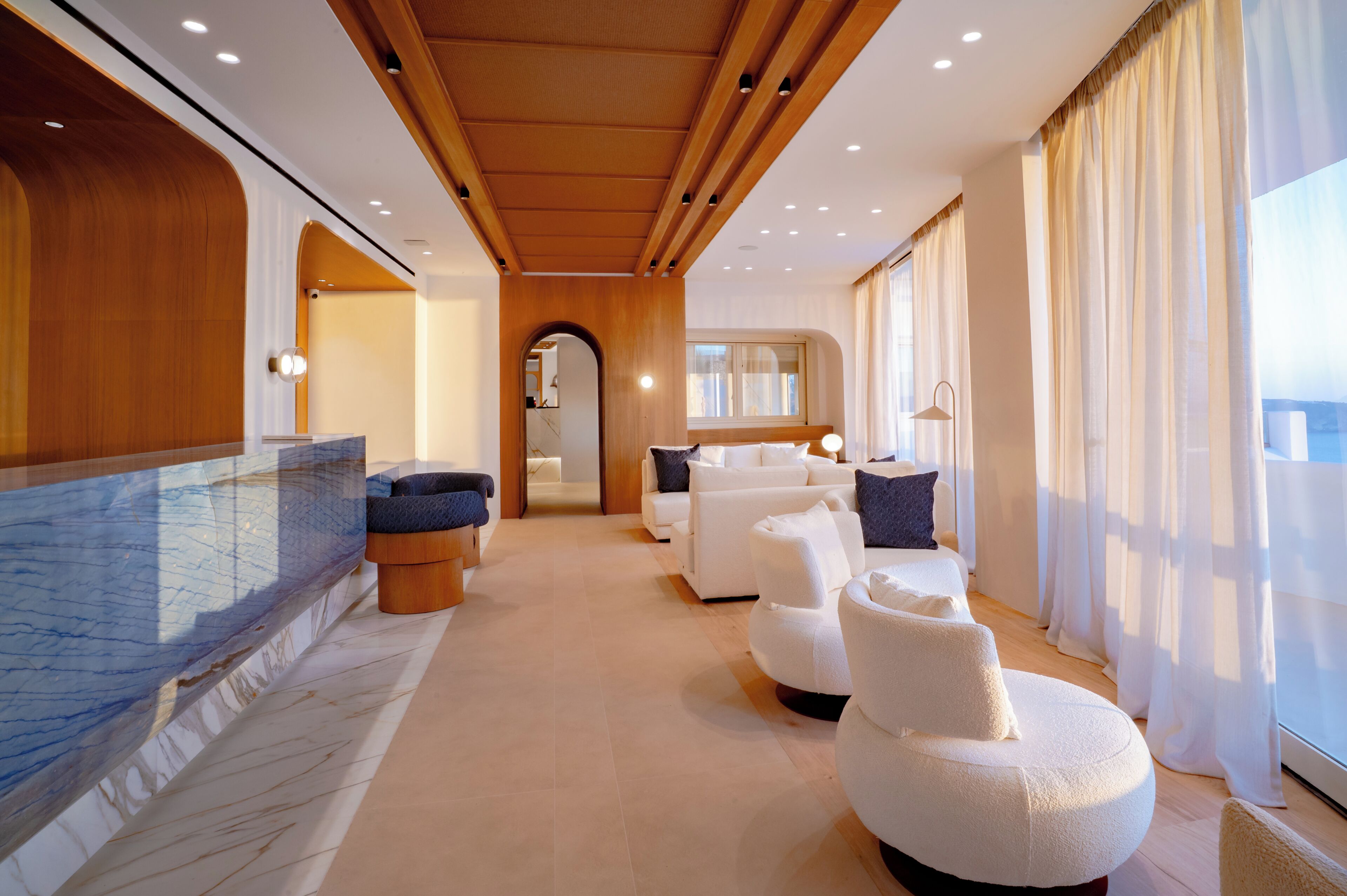 A modern interior with a marble wall, wooden ceiling, and a seating area with white sofas and a massage chair.