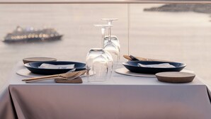 A table set for dining with a view of the sea and a ship in the distance. - Apeiron Blue by Apeiron Hotels (Santorini)