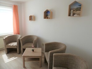 A room with two armchairs, a small wooden table, and three wall-mounted shelves with decorative items.