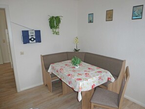 Ein Essbereich mit Tisch, der mit einer blumigen Tischdecke bedeckt ist, zwei Stühlen, einer Topfpflanze und Wandbildern.