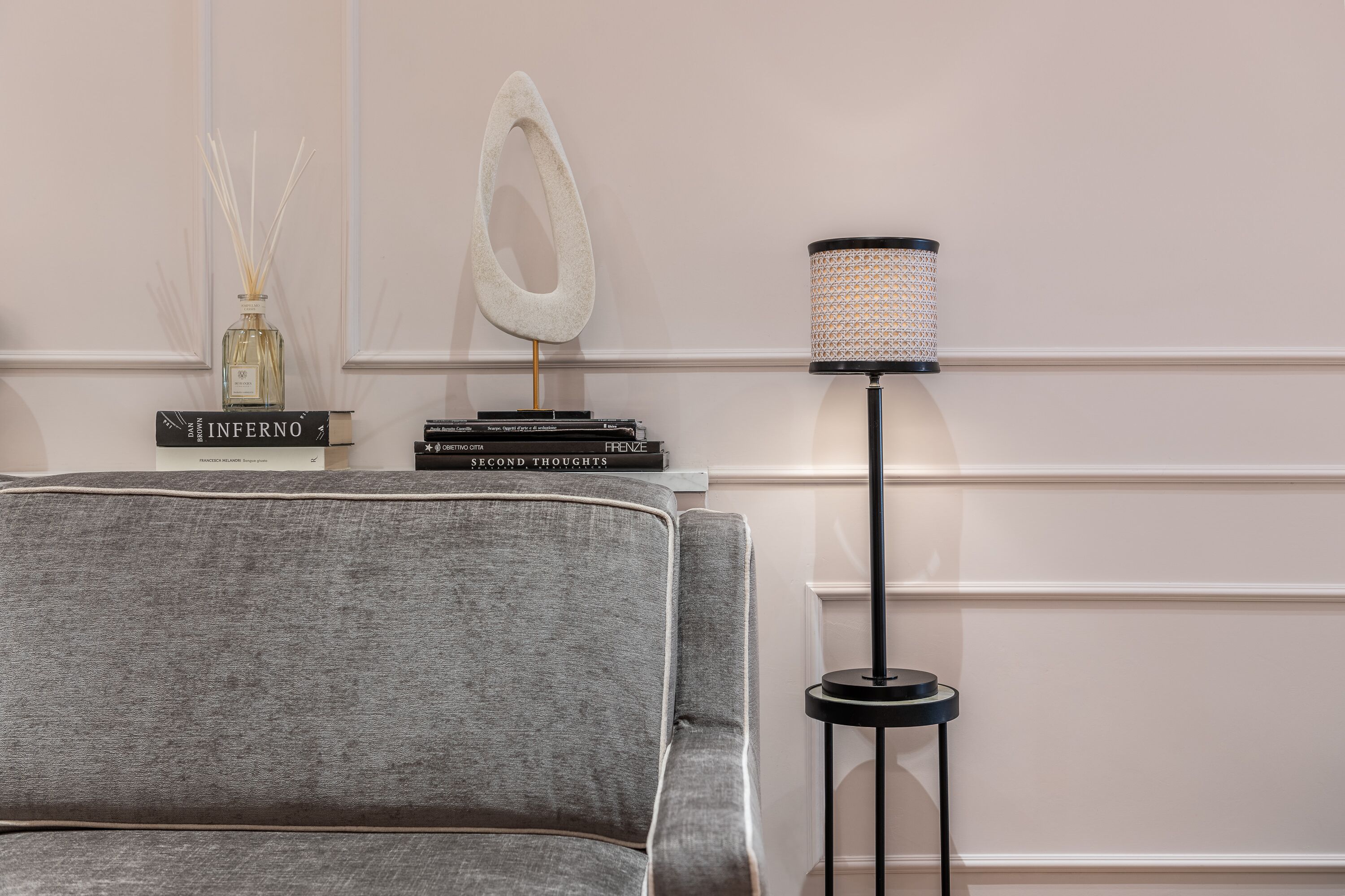 Un fauteuil à revêtement gris, un grand lampadaire avec un abat-jour à motifs et une pile de livres sur un mur blanc.