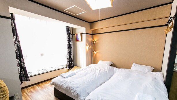 Ein Hotelzimmer mit einem großen Bett, einem fensterbelaubten Fenster, einem Nachttisch und einer Wandleuchte.