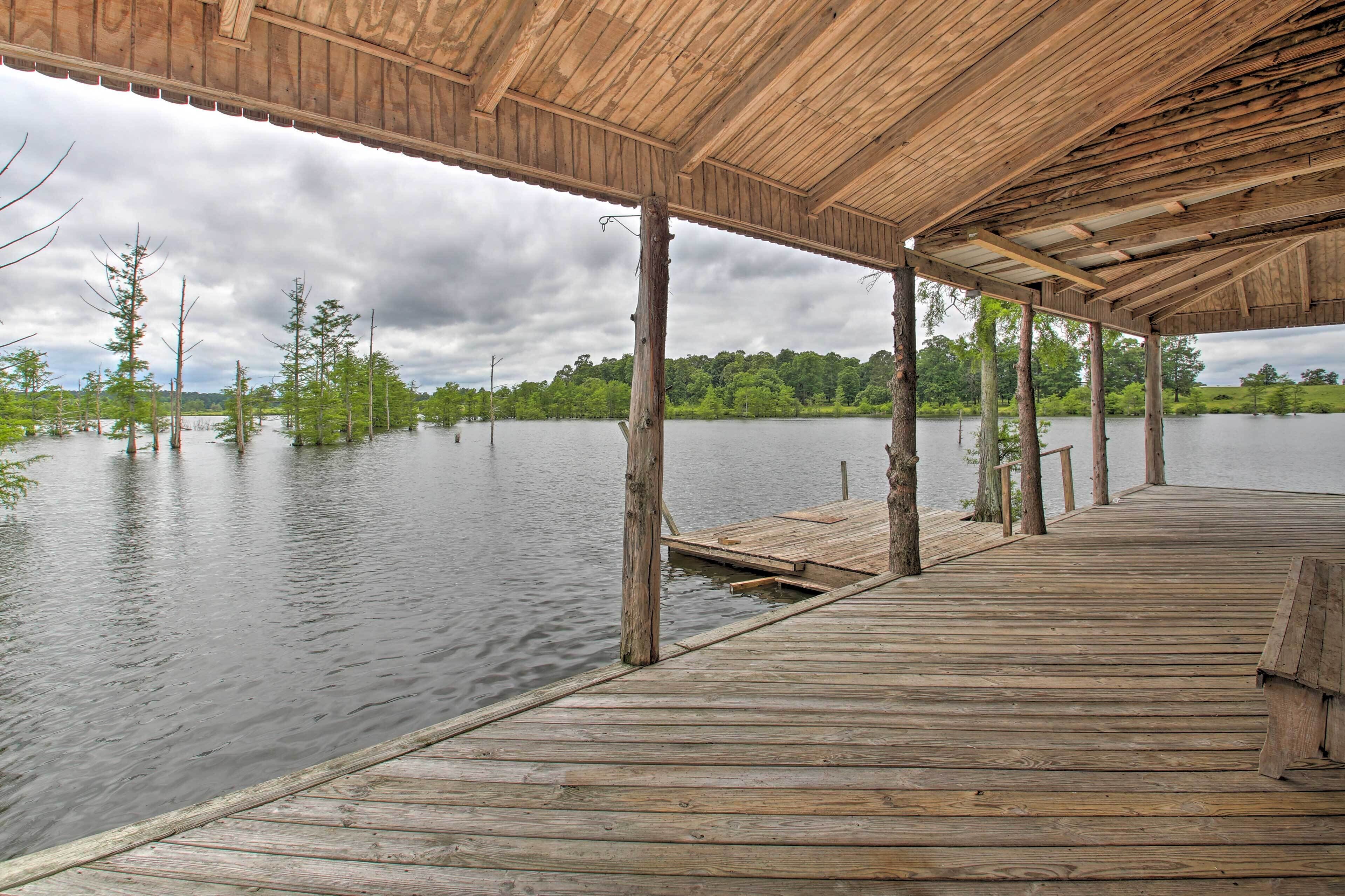 A wooden pier extending into a calm lake, supported by wooden posts, with a covered area overhead.