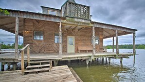 A wooden cabin with a covered deck extending over water, featuring a door and windows. - Secluded Angler's Haven - Boat + Fish! (Rosston)