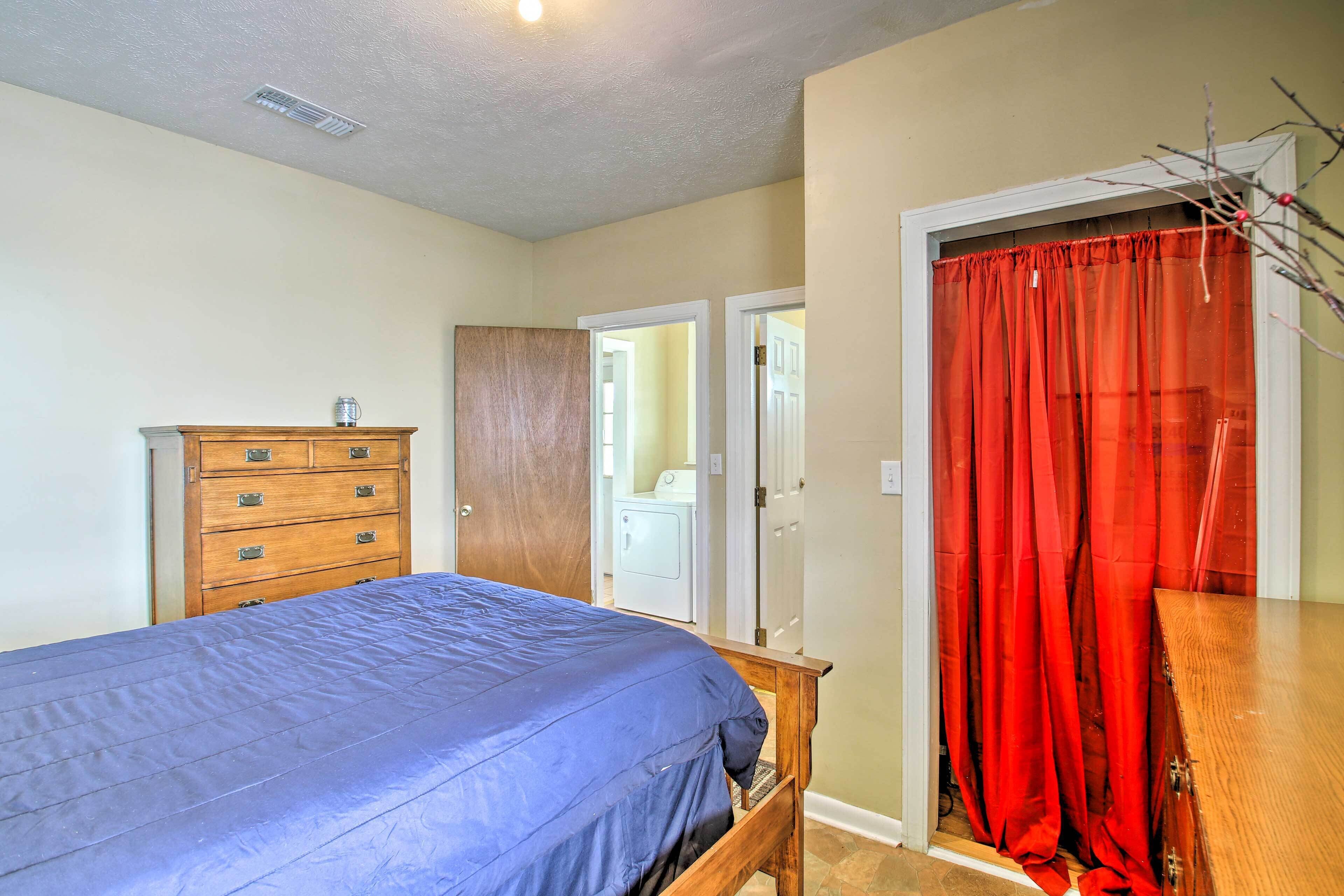 Un dormitorio con cama, cómoda de madera y cortina roja.