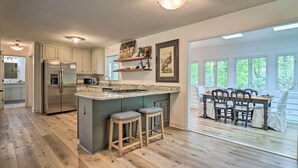 Una cocina moderna con una isla central, taburetes de bar de madera y una zona de comedor con mesa y sillas.