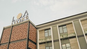 A modern building with a geometric facade, a prominent sign with the name 'A' and 'ING', and a section with vertical windows and greenery. - LOA Living Solo Baru (Grogol)