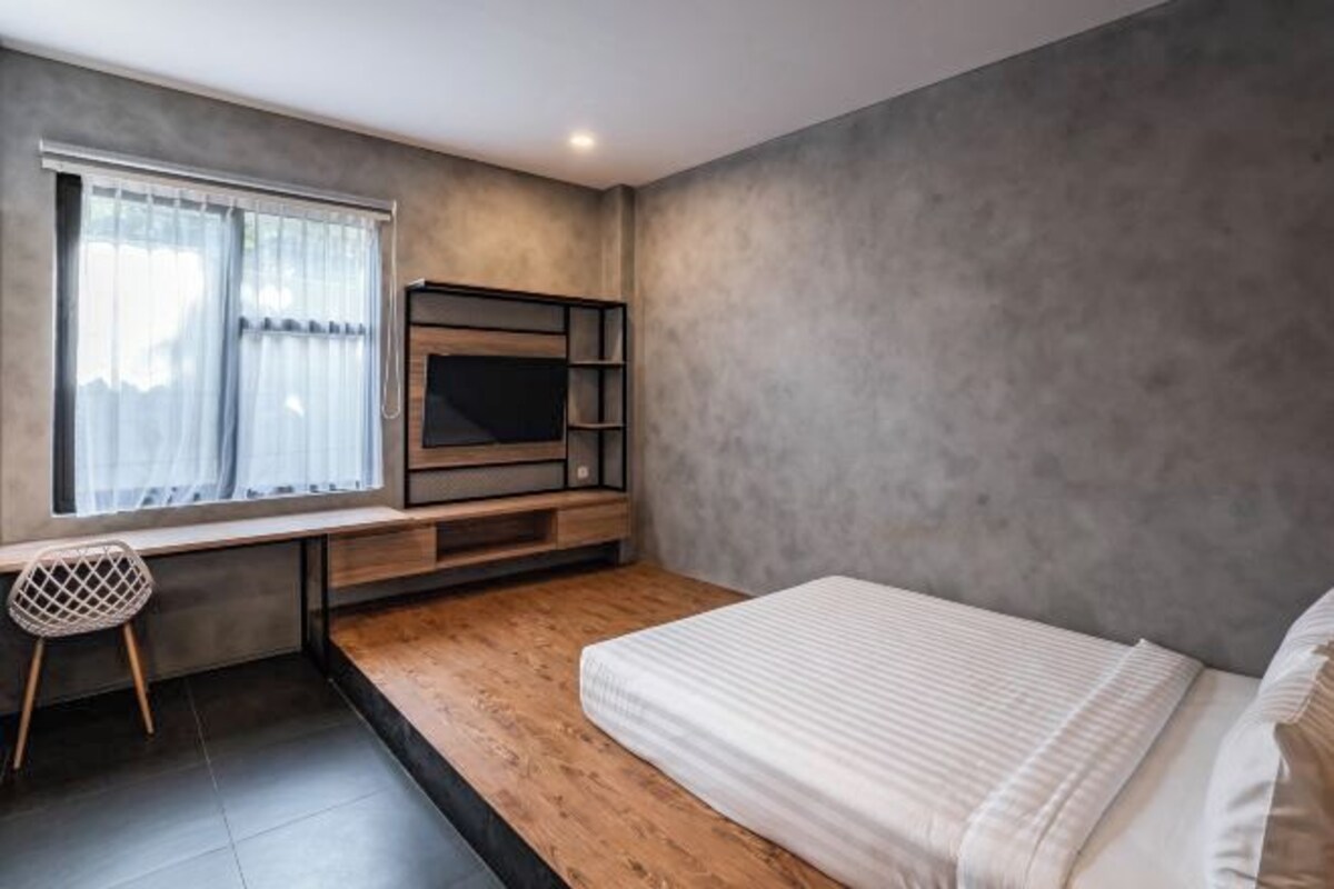 A modern bedroom with a bed, a TV mounted on the wall, a desk with a chair, and a window with curtains.