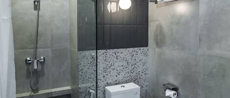 A modern bathroom with a glass-enclosed shower, a toilet, and a sink with a marble countertop.