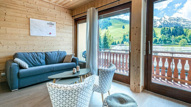 A wooden interior with a sofa, patterned chairs, a table, and a balcony with a mountain view. - Large Studio Cabin, Balcony, Parking, La Clusaz Center (La Clusaz)