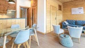 A modern interior with a wooden ceiling, a glass dining table with chairs, a blue sofa, patterned ottomans, and a wooden cabinet. - Large Studio Cabin, Balcony, Parking, La Clusaz Center (La Clusaz)