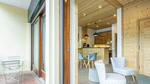 A modern interior with wooden ceiling beams, a dining area with blue chairs, and a kitchen with wooden cabinets. - Large Studio Cabin, Balcony, Parking, La Clusaz Center (La Clusaz)