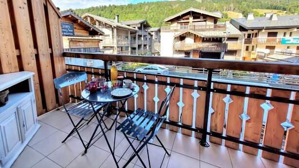A balcony with a table and chairs, overlooking a village with traditional buildings and a forested hill. - Central studio, near slopes, ideal for 2 (Les Gets)