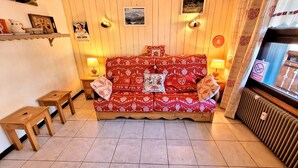 A cozy living room with a red patterned sofa, two small wooden tables, and a radiator. - Central studio, near slopes, ideal for 2 (Les Gets)