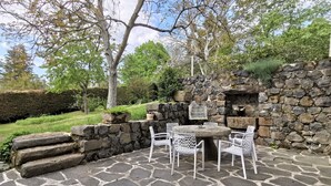 An outdoor patio with stone flooring, white metal chairs, a round table, and a stone wall with a birdcage.