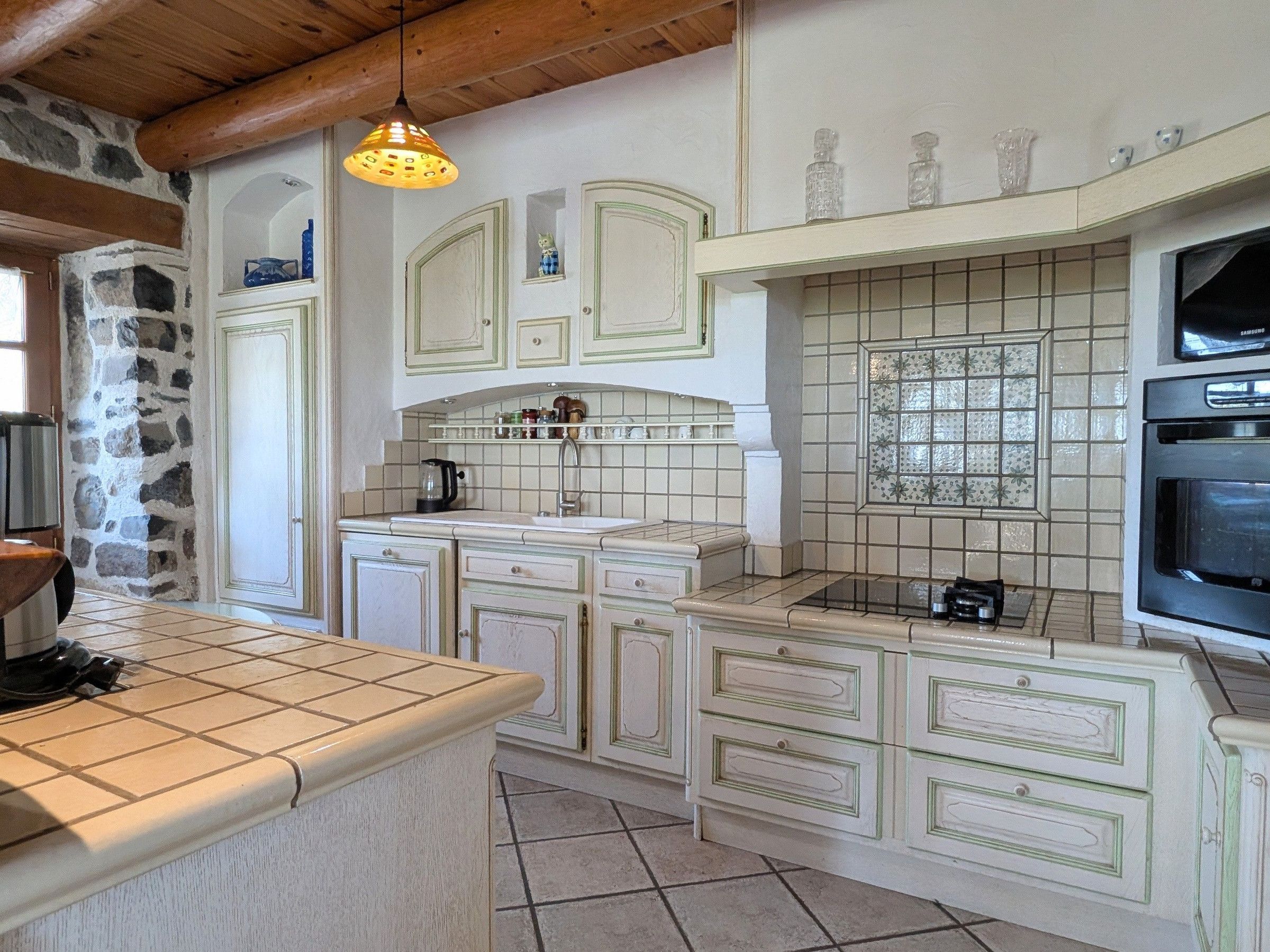 Cocina con armarios blancos, salpicadero de azulejos, horno empotrado y lámpara colgante.