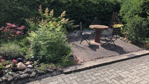 Un'area giardino con un tavolo in pietra e due sedie, circondata da diverse piante e un muro in pietra.