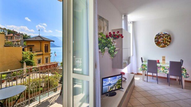 A balcony with a table and chairs, a TV, and a view of the sea. - Casa Lido beautiful lake view (Varenna)