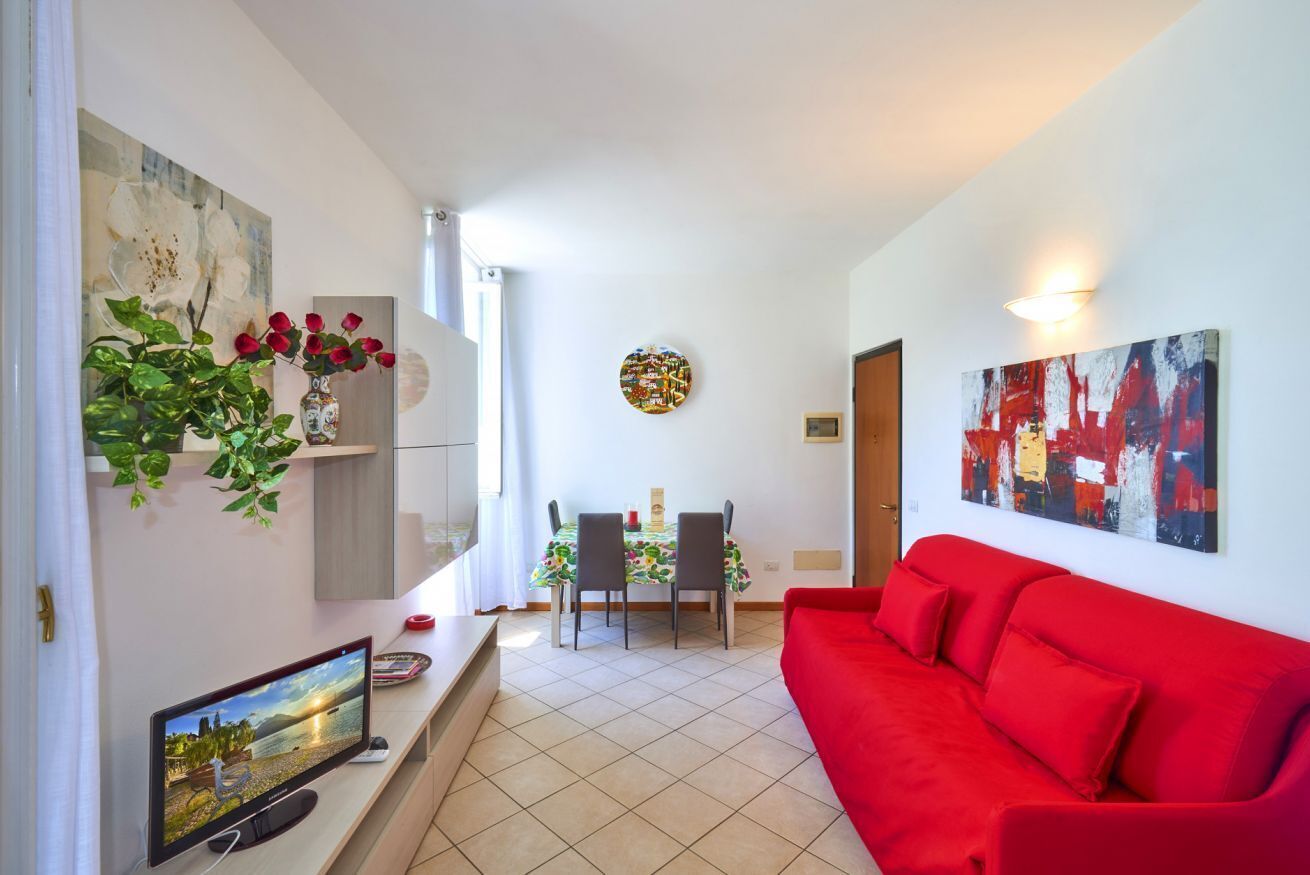 Ein modernes Wohnzimmer mit einem roten Sofa, einem Flachbildfernseher, einer Essecke mit Tisch und Stühlen sowie Kunstwerken an den Wänden.